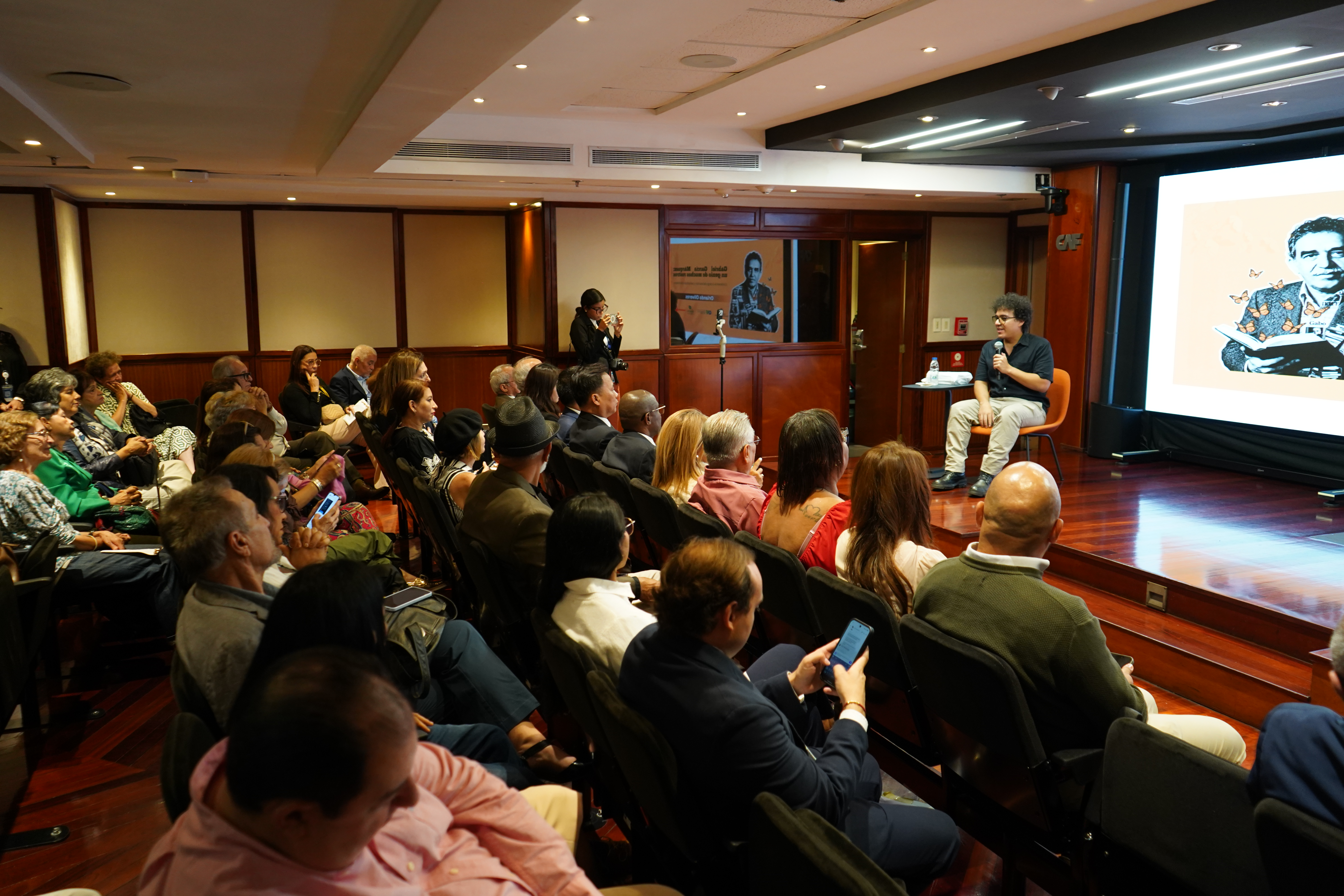 El escritor y periodista cultural colombiano Orlando Oliveros durante su conferencia en el auditorio de CAF, acompañado por el público asistente.