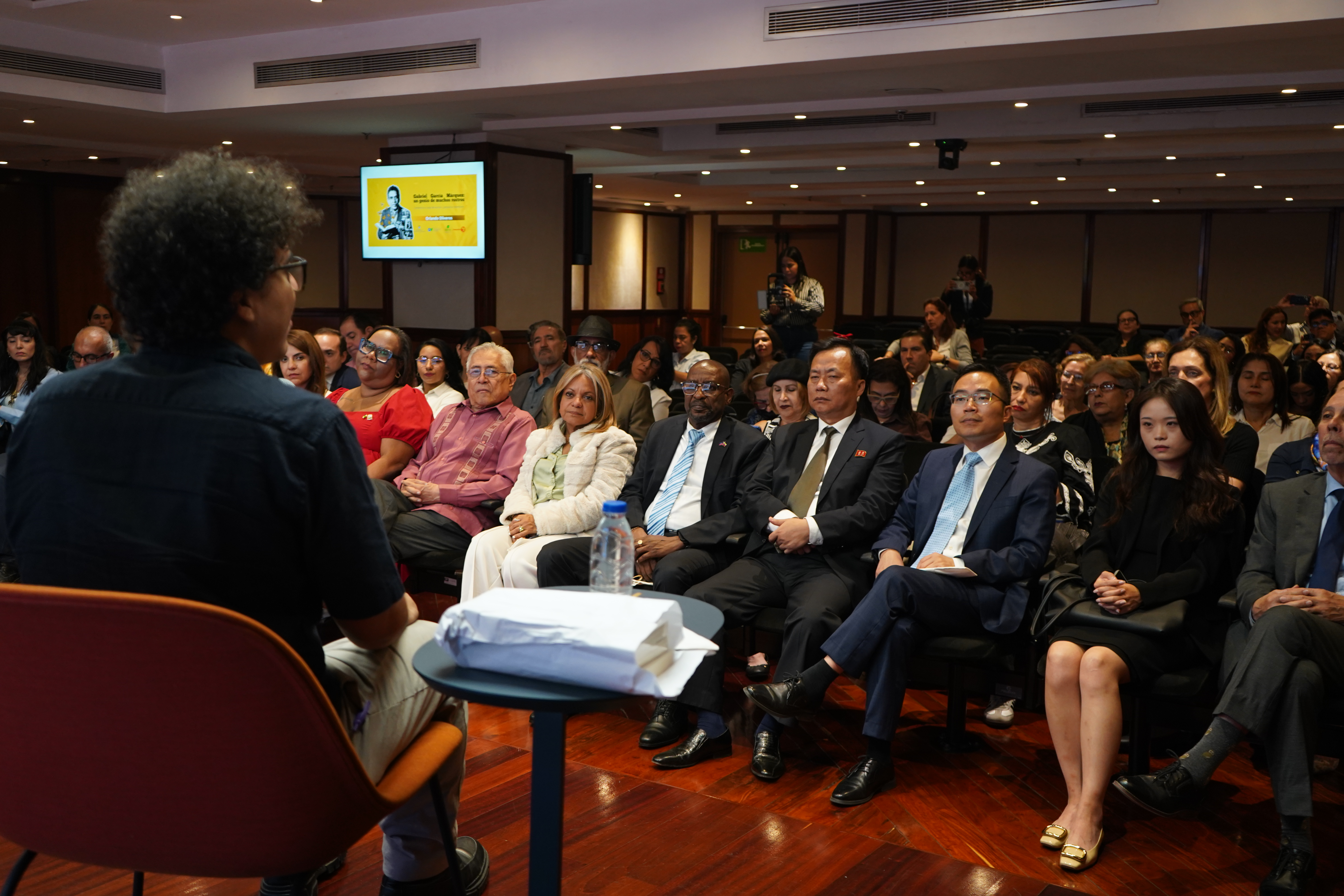 El escritor y periodista cultural colombiano Orlando Oliveros durante su conferencia en el auditorio de CAF, acompañado por el público asistente.